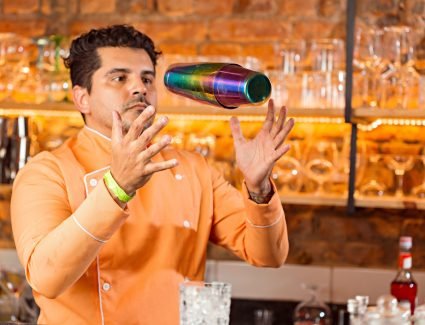pexels photo 14161989 14161989 A professional bartender tosses a colorful cocktail shaker in a vibrant bar setting.